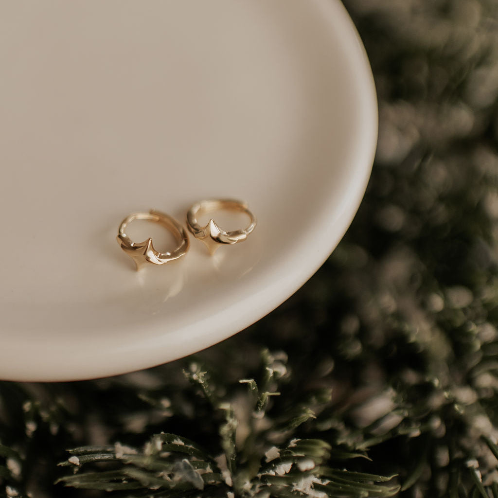 Gold earrings on a white dish with a blurred green background