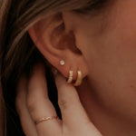 Close-up of an ear with gold hoop earrings and diamond studs and a hand adjusting them.