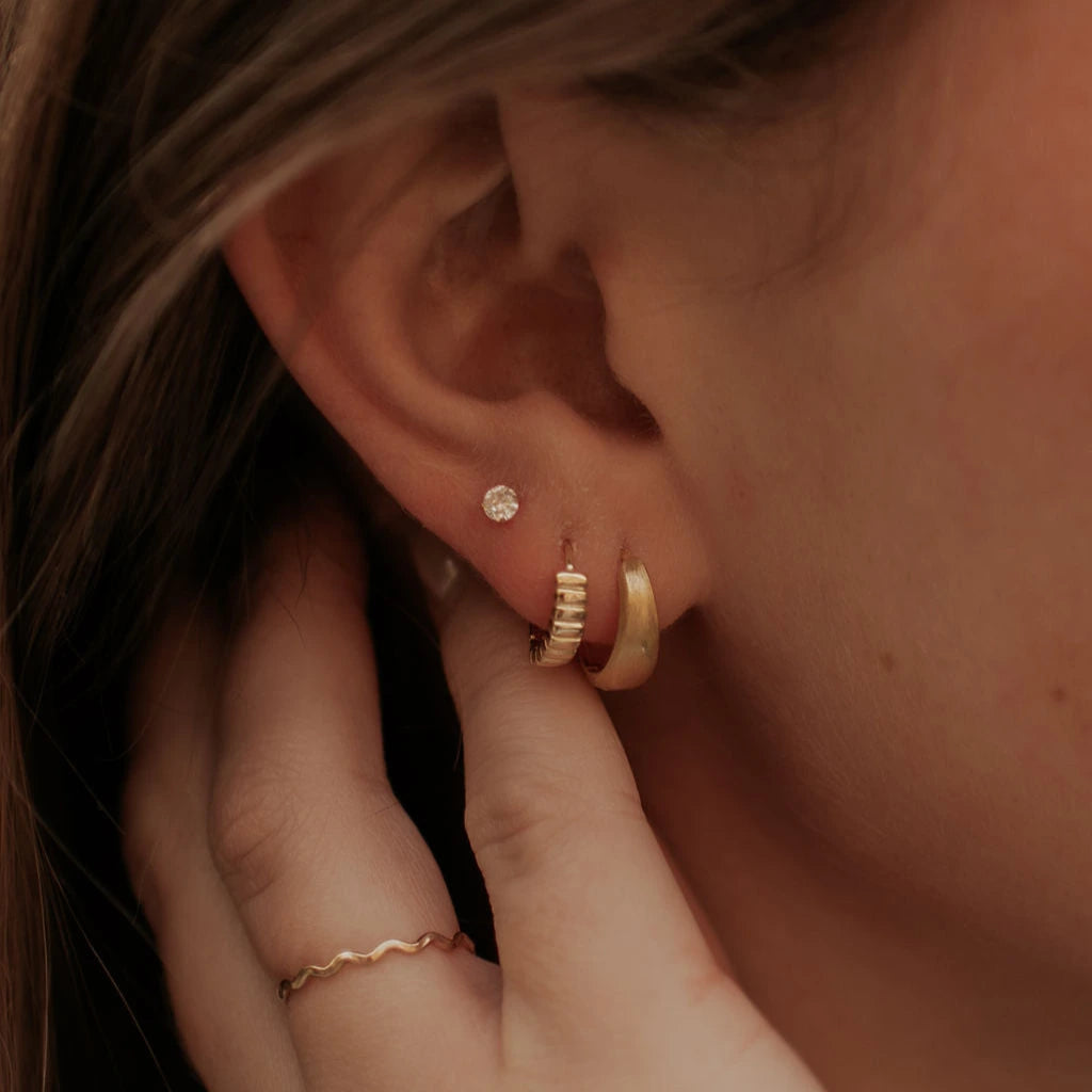 Close-up of an ear with gold hoop earrings and diamond studs and a hand adjusting them.