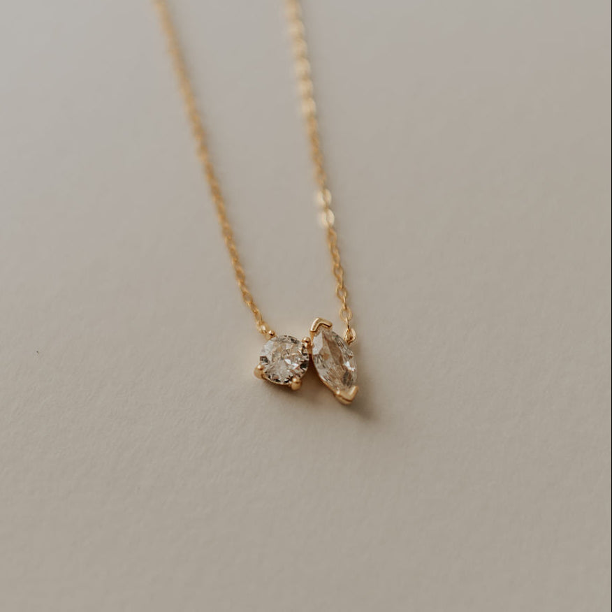 Gold necklace with a diamond pendant on a neutral background