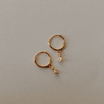 Gold hoop earrings with small diamond-shaped charms on a light gray background