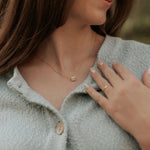 Woman wearing a delicate necklace with a small pendant, close-up of her neck and hand.