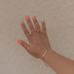 Hand with orange nail polish and gold rings on a beige background