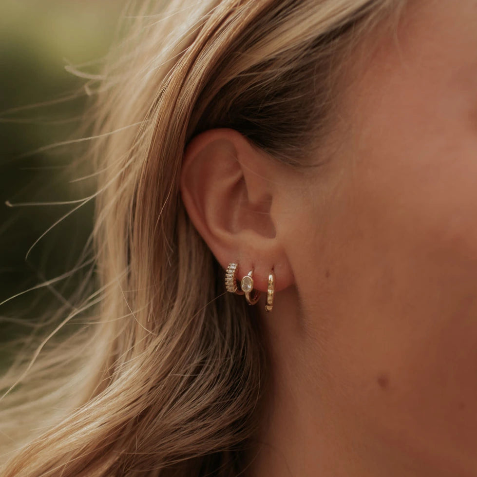 Close-up of an ear wearing gold hoop earrings with blurred hair and background