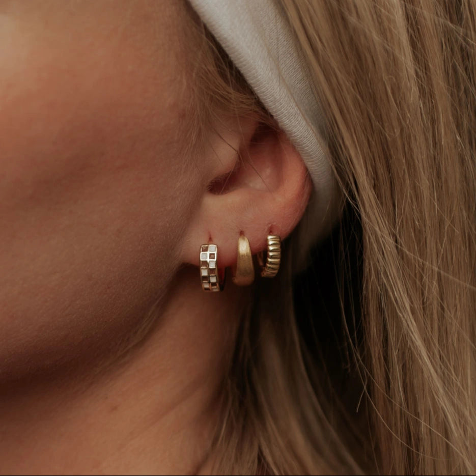Close-up of an ear wearing gold hoop earrings with a neutral background