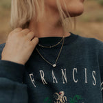 Person wearing a dark blue sweatshirt adjusting a necklace.