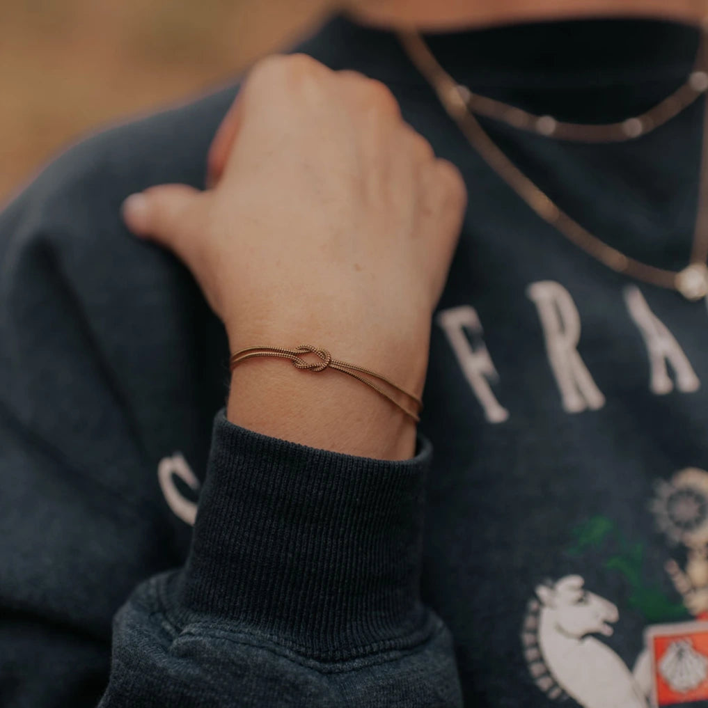 Close-up of a person wearing a dark blue sweater with visible branding, focusing on a bracelet on their wrist.