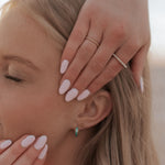 Load image into Gallery viewer, Close-up of a woman with light makeup, wearing gold and green earrings, and gold rings on her fingers.
