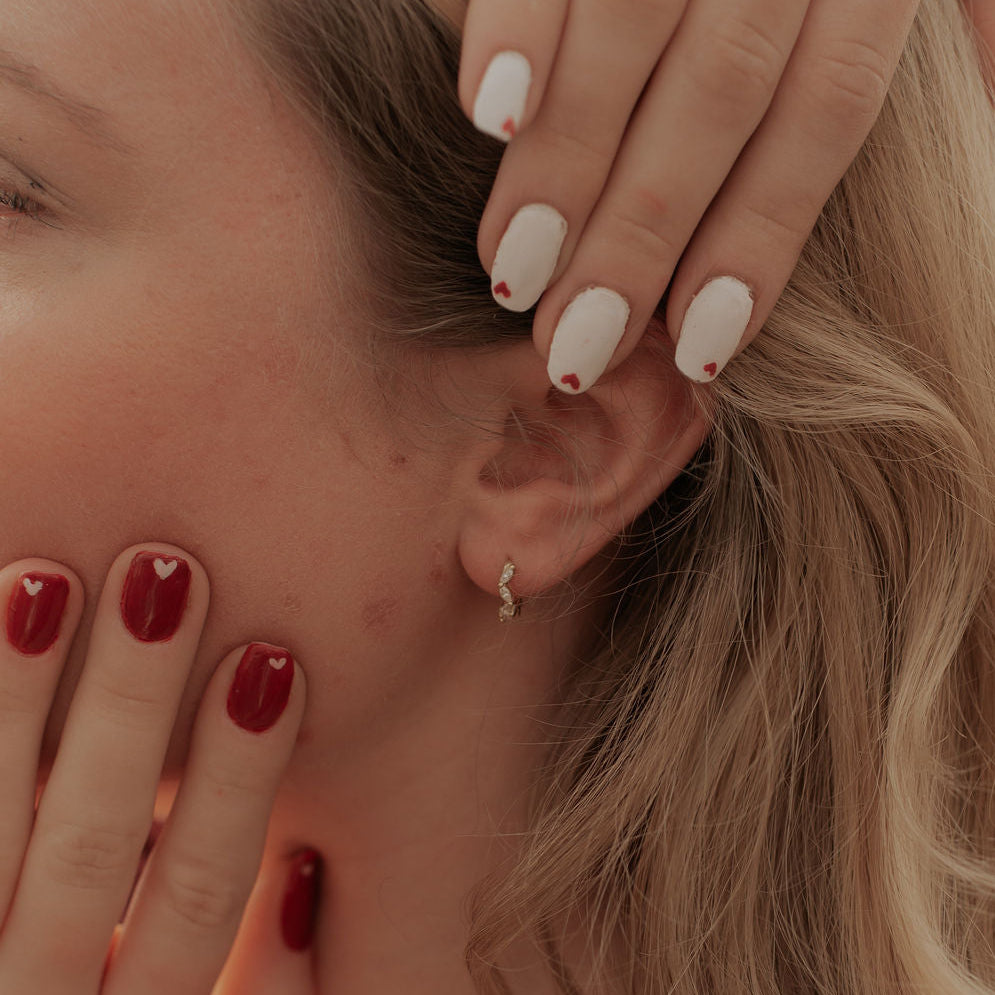 Close-up of a person with red nail polish touching their face, wearing a floral top.