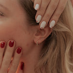 Close-up of a person with red nail polish touching their face, wearing a floral top.
