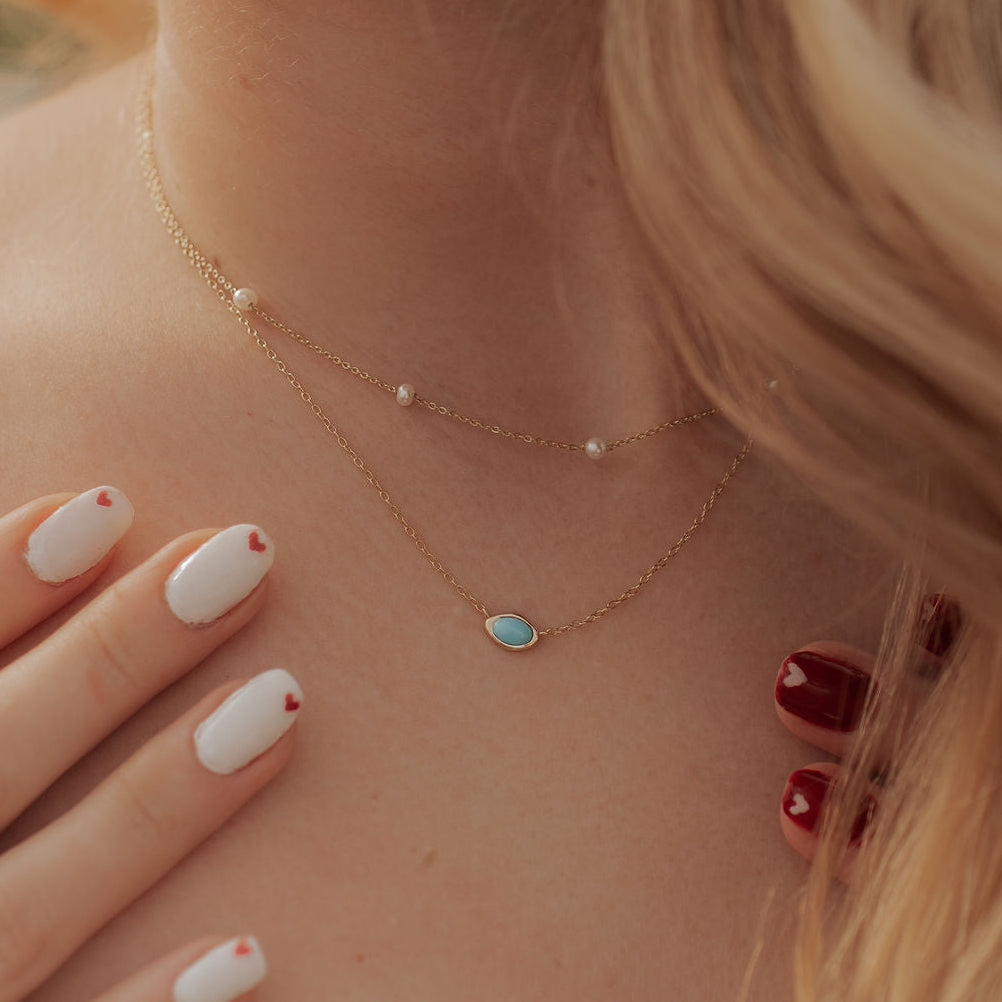 Close-up of a person wearing a delicate turquoise necklace with a blurred background