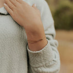 Close-up of a hand wearing a gold bracelet with a blurred background