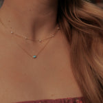 Close-up of a necklace with a turquoise pendant on a person with long hair.