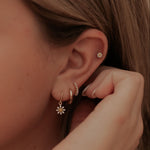 Load image into Gallery viewer, Close-up of a person wearing gold earrings with floral designs.
