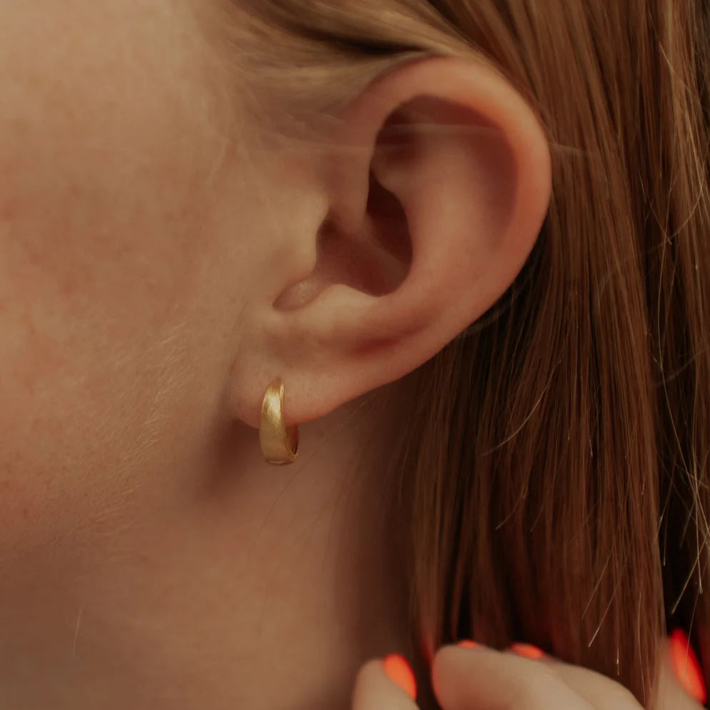 Close-up of a person wearing a gold hoop earring.