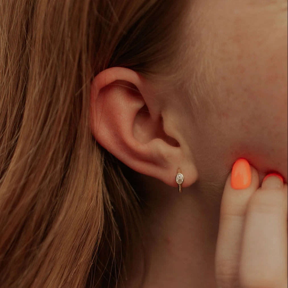 Close-up of a person's ear with an earring and a hand holding a red object near the ear.