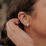 Close-up of an ear wearing a gold hoop earring with a dragonfly detail.