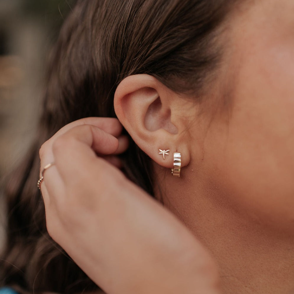 Close-up of an ear wearing a gold hoop earring with a dragonfly detail.