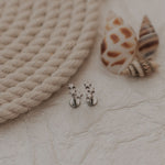 Load image into Gallery viewer, Pair of silver star earrings on a textured surface with a rope and shell in the background.

