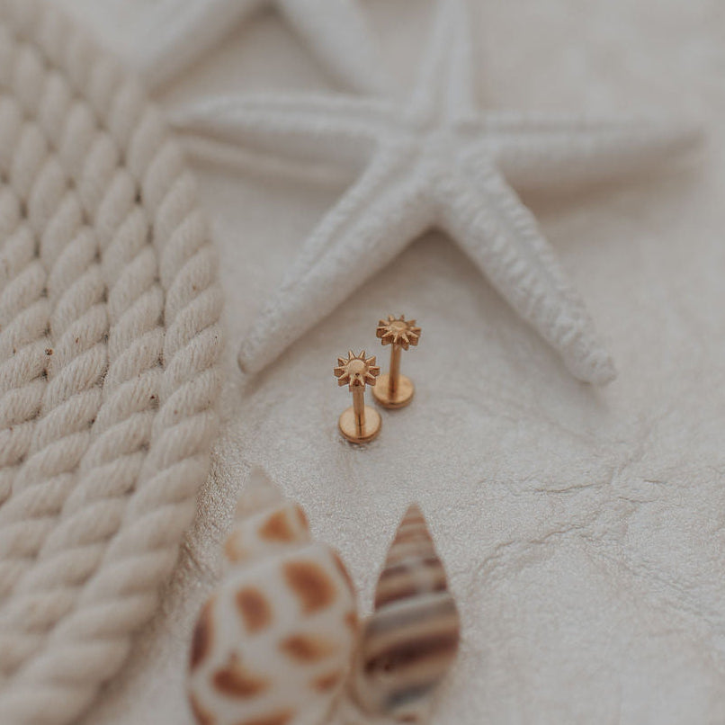 Gold sunshine earrings on a textured beige surface with starfish and rope.