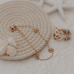 Load image into Gallery viewer, Gold bracelet with floral designs on a textured surface with shells and starfish.
