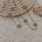 Two bracelets with flower-shaped pendants on a textured surface with seashells.
