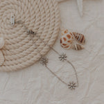 Load image into Gallery viewer, Silver flower-shaped earring on a textured surface with rope and shells
