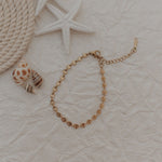 Gold bracelet on a textured beige surface with starfish and rope