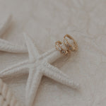 Load image into Gallery viewer, Gold star earrings on a starfish with a textured beige background
