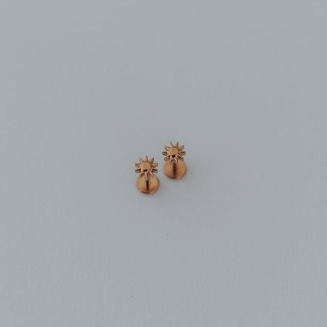 Small gold sun earring on a light gray background