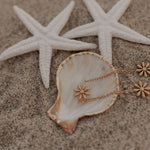 Load image into Gallery viewer, Gold bracelet with floral pendants on a shell and starfish on sand
