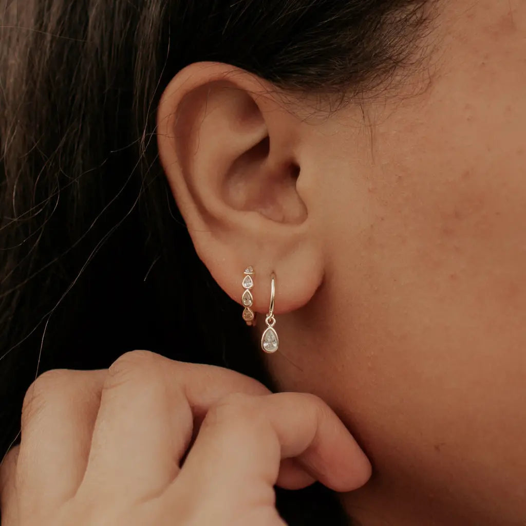 Close-up of a person wearing a gold earring with three small stones.