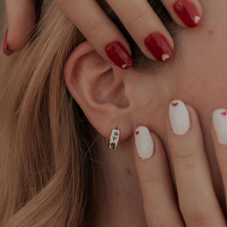 Close-up of a person's ear with earrings, hand touching hair, and various nail colors.