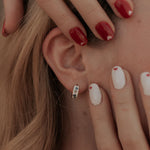 Load image into Gallery viewer, Close-up of a person's ear with earrings, hand touching hair, and various nail colors.
