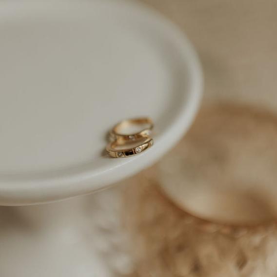 Two gold earings on a white dish with a blurred background