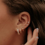 Close-up of an ear with multiple diamond earrings and a hand adjusting her hair. 