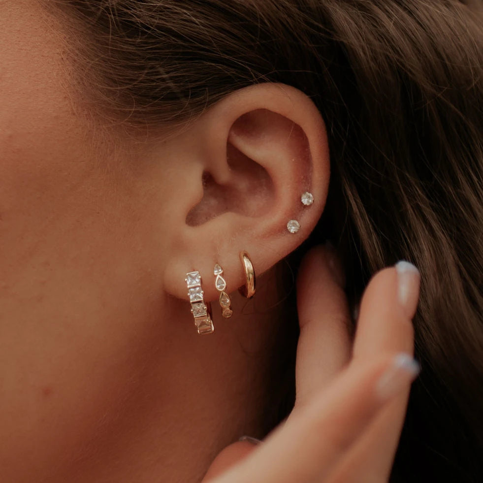 Close-up of an ear with multiple diamond earrings and a hand adjusting them.