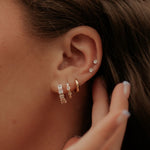 Close-up of an ear with multiple diamond earrings and a hand adjusting them.