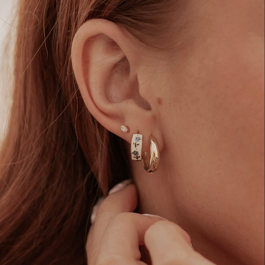 Close-up of a person wearing gold hoop earrings with a blurred background