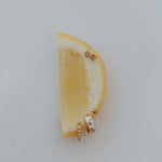 A pair of gold-toned stud earrings with floral enamel details, displayed on a yellow lemon wedge against a light gray background.