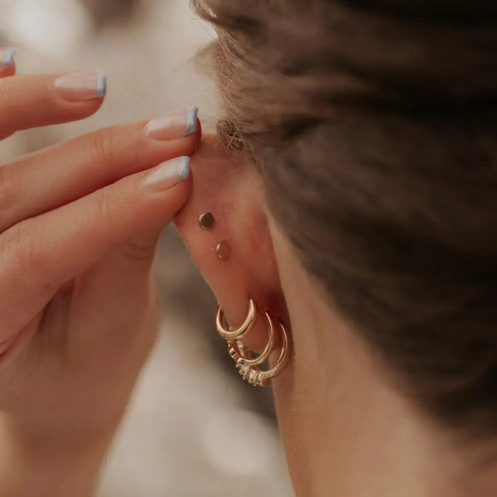 Close-up of a person wearing gold hoop earrings with a blurred background