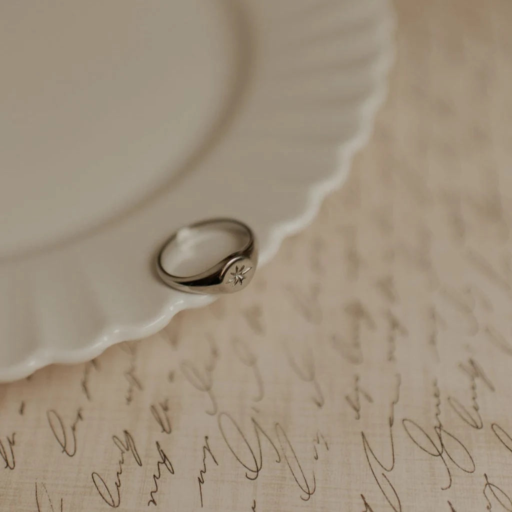 Silver ring with a small diamond shape on a textured beige surface