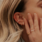 Close-up of an ear with gold hoop earrings and a hand wearing rings.