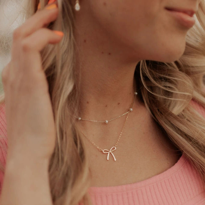 Close-up of a woman wearing a delicate necklace with a bow pendant.