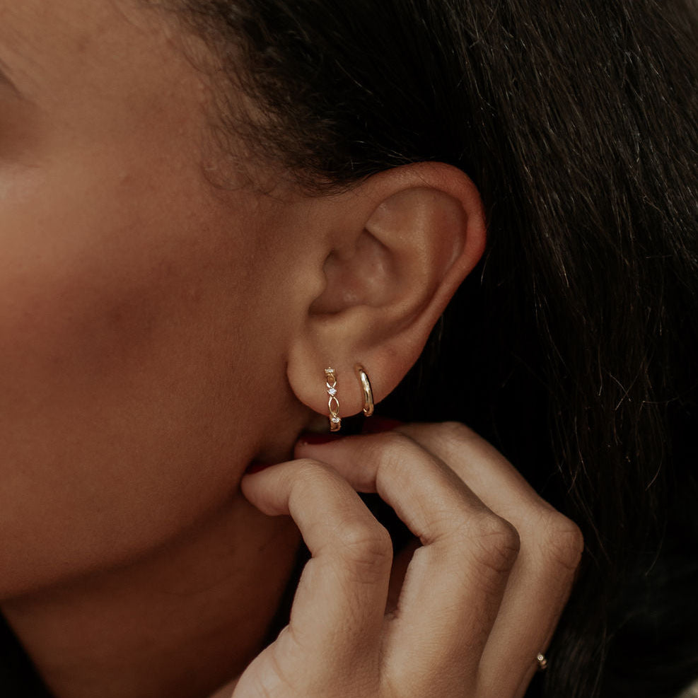 Close-up of an ear with gold hoop earrings and a hand adjusting hair.