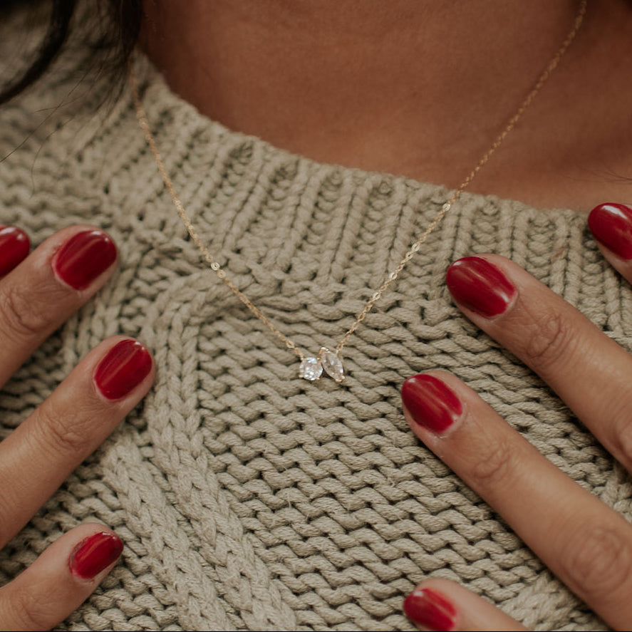 Close-up of a person wearing a diamond necklace on a beige knitted sweater.