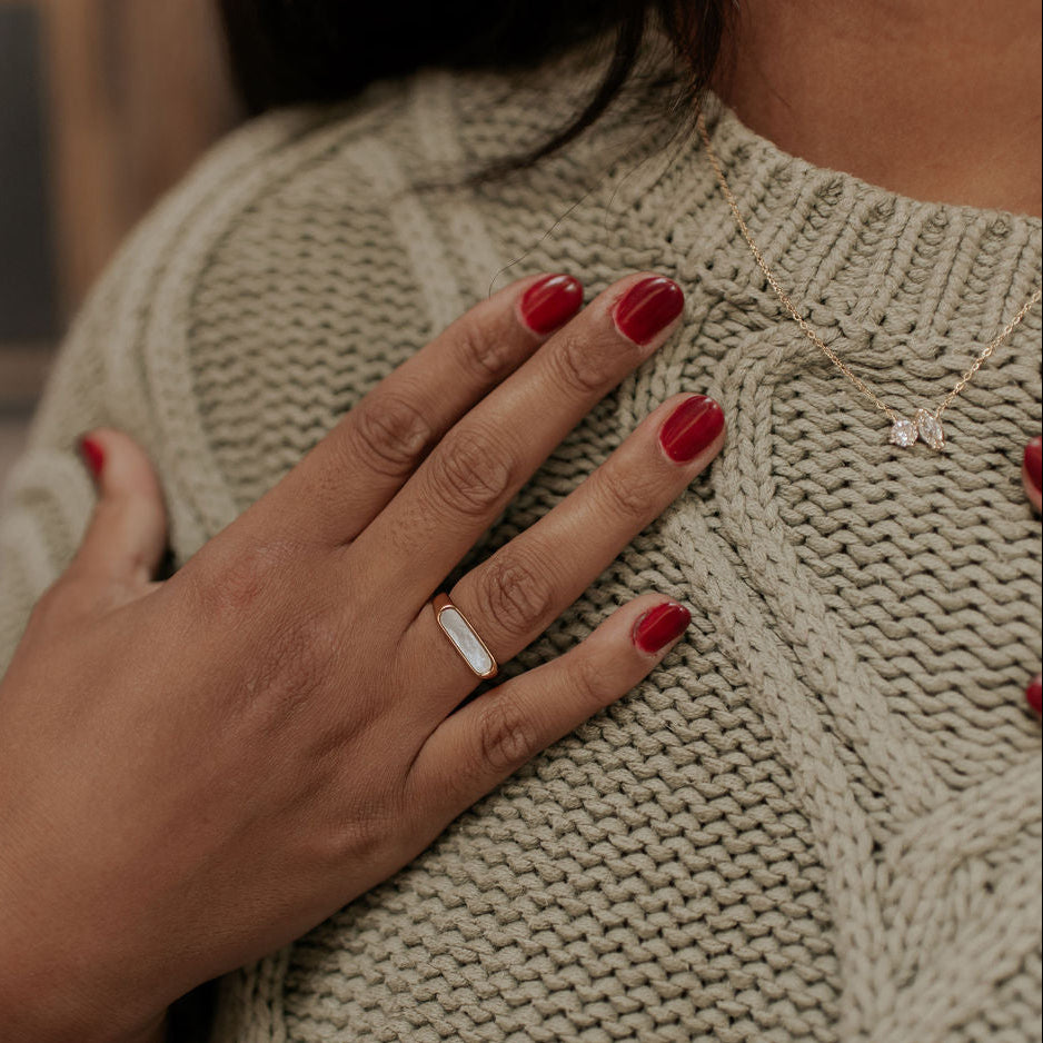 Person wearing a beige knitted sweater with a close-up of their hand and ring.