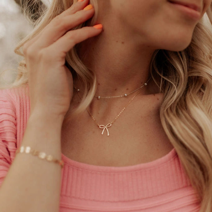 Woman wearing a gold bow necklace with a blurred background