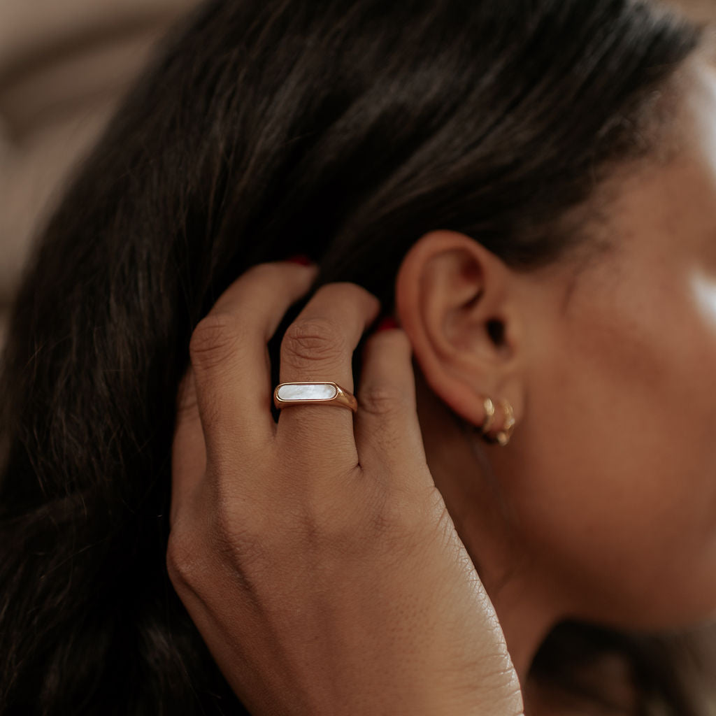 Close-up of a person wearing gold jewelry including an earring, ring, and bracelet.