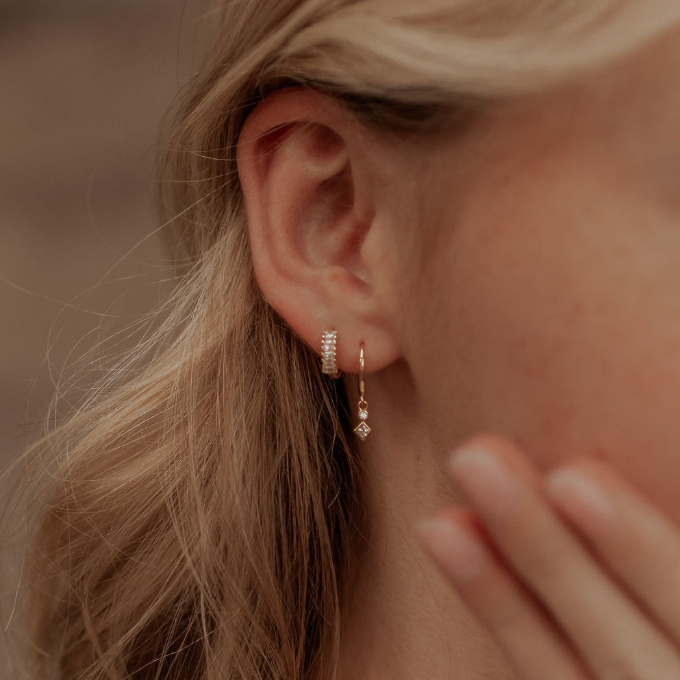 Close-up of a person wearing gold earrings with a blurred background